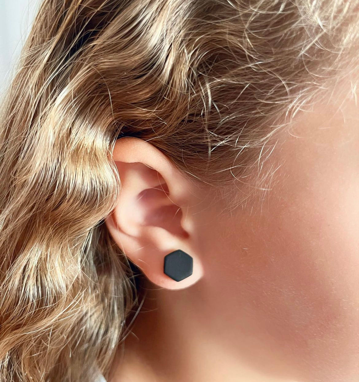 model wearing a 10mm black hexagon stud earrings handmade from polymer clay by Vertseas for size reference