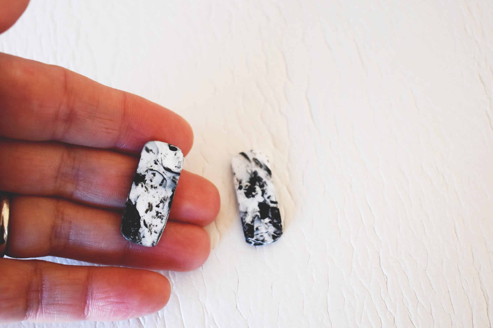 Hands showing a black and white marble effect rectangle stud earrings handmade from polymer clay by Vertseas