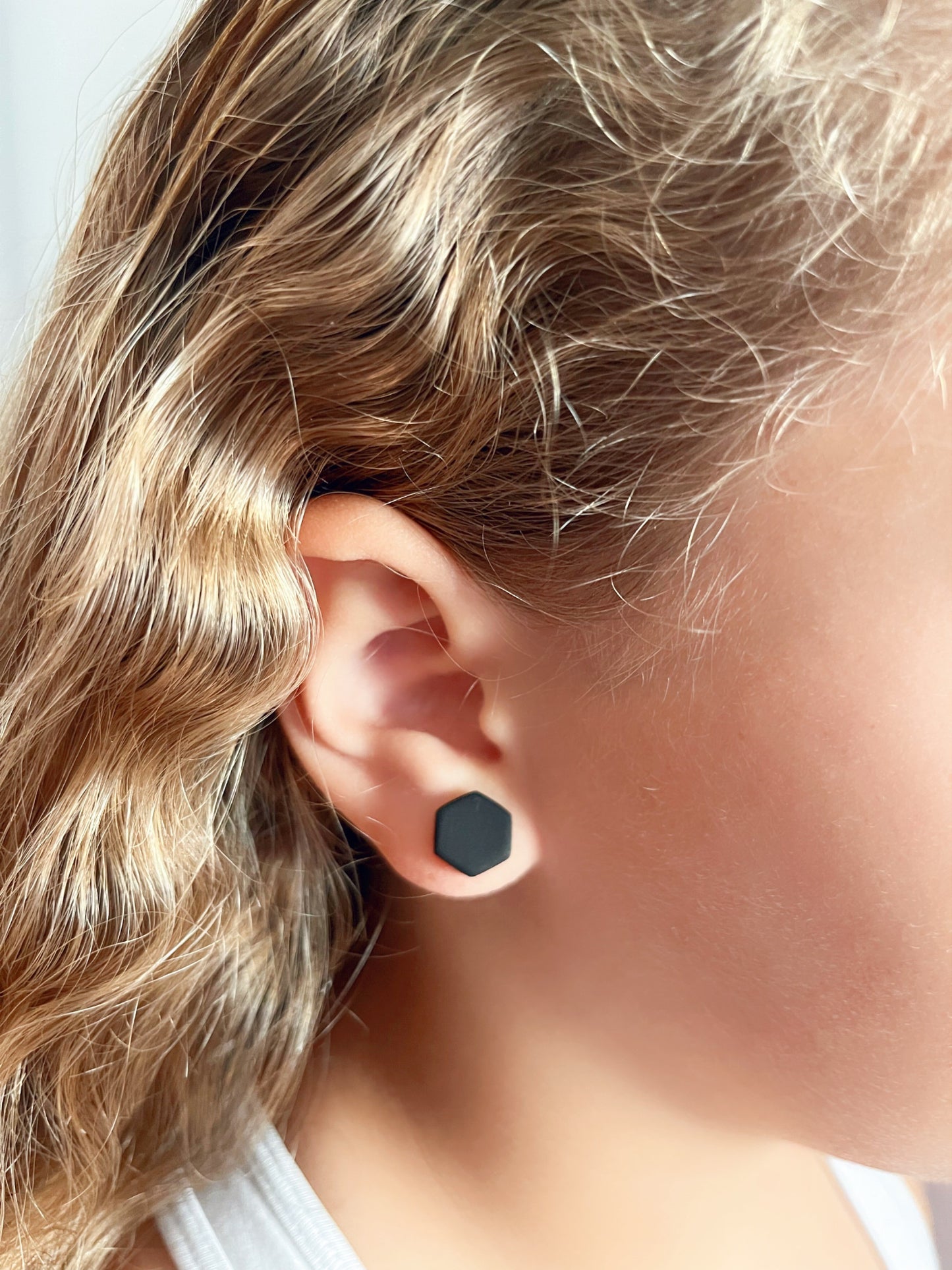 Model wearing a 10mm matte black hexagon stud earrings handmade from polymer clay by Vertseas.